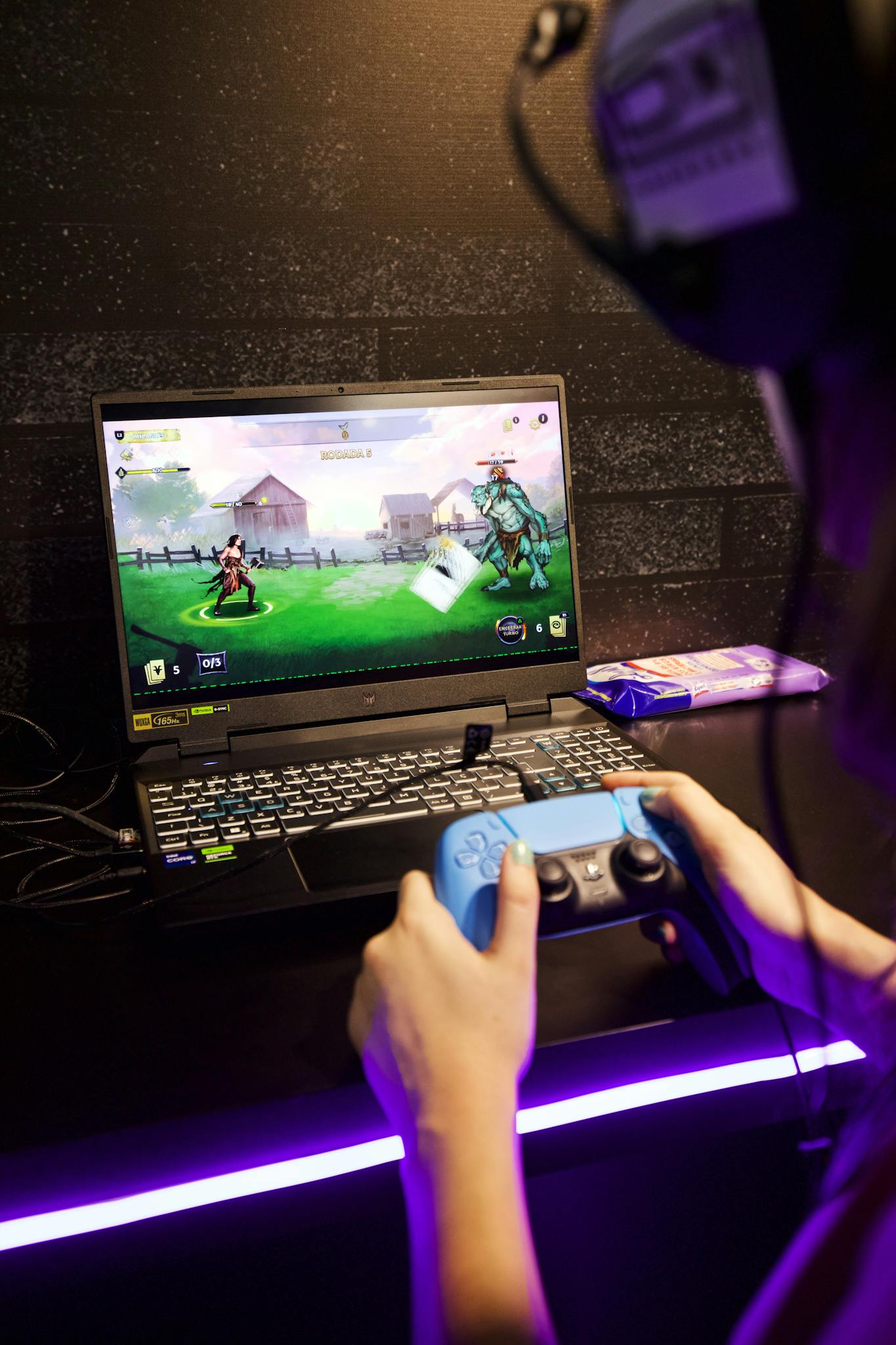 A person using a blue controller and headphones to play an interactive video game on a laptop.
